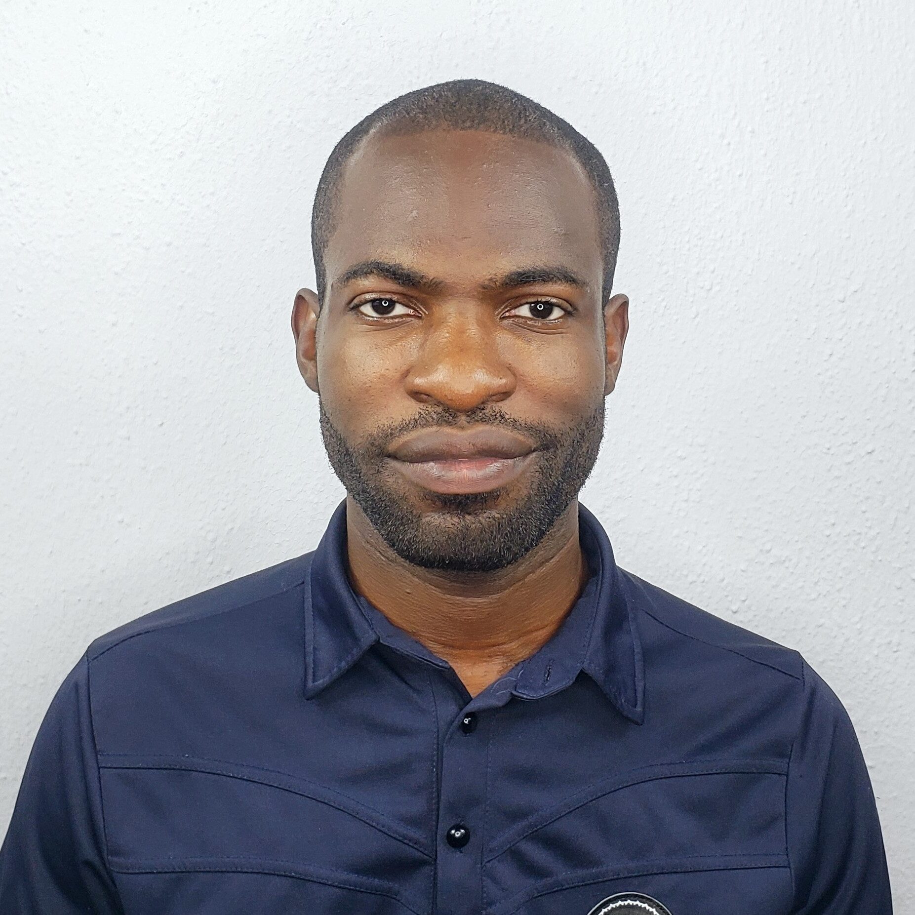 Headshot of Chukwuma John Okolie, portrait of a black hair man with a short black beard wearing a blue polo.