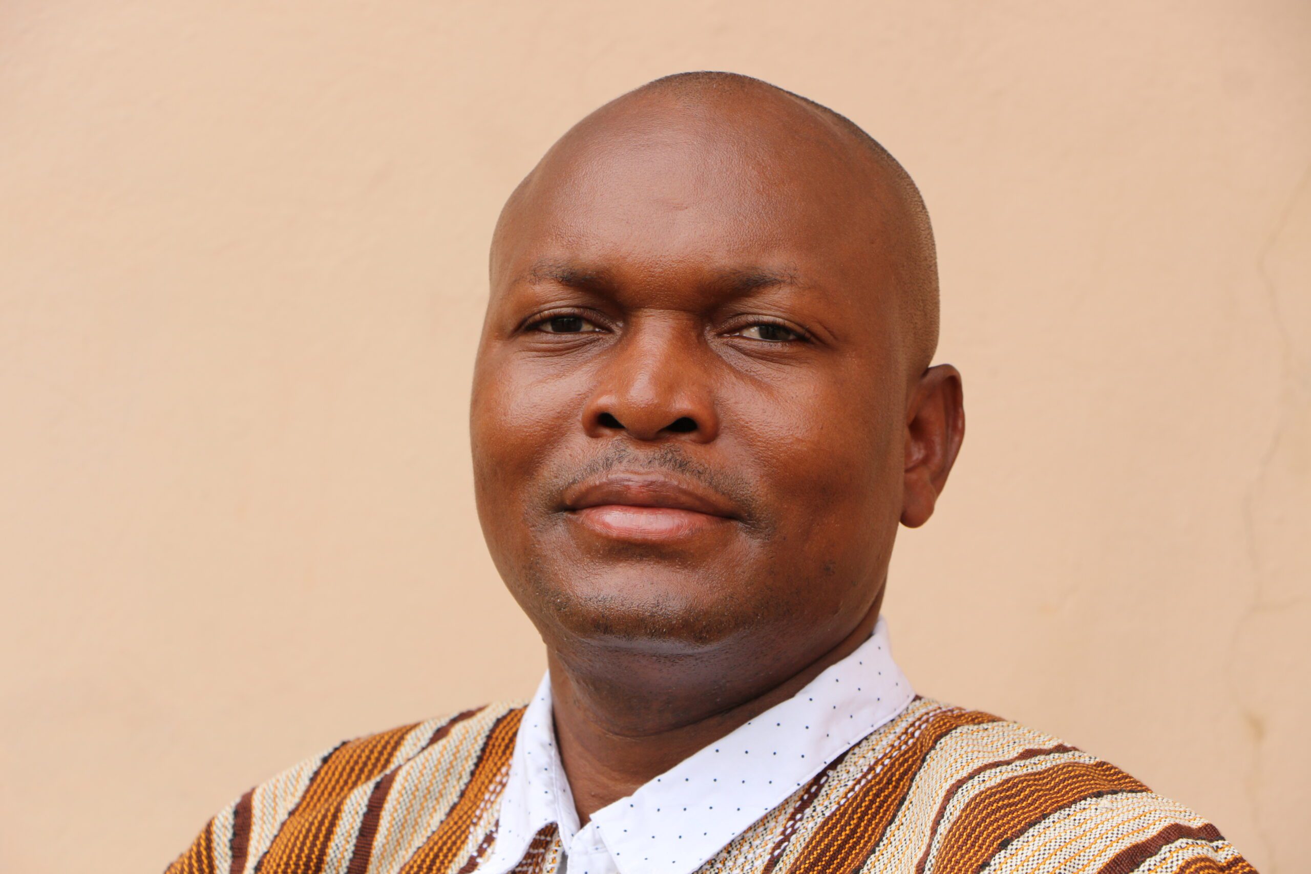 Headshot of Kusimi John Manyimadin, a bold man smiling at the camera.