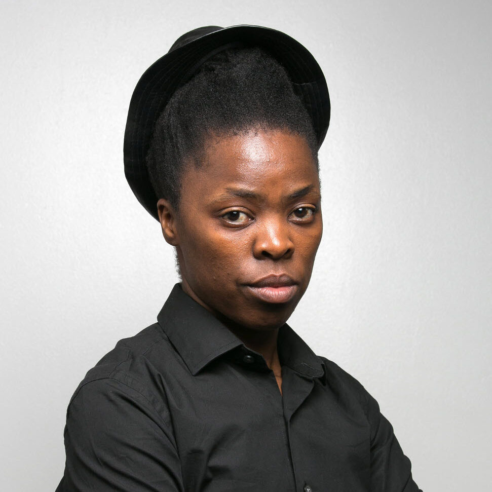 Portrait of Zanele Muholi, headshot of a woman with black hair wearing a black shirt and crossing her arms.