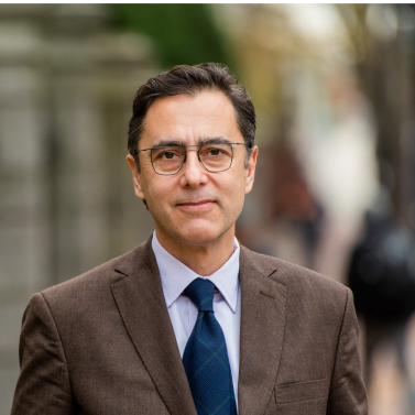 Portrait of a man with short hair, wearing glasses a tie and a suit. Portrait of George Sarrinikolaou.