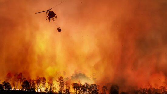 Panoramic view of a forest fire being put out by a helicopter carrying water.