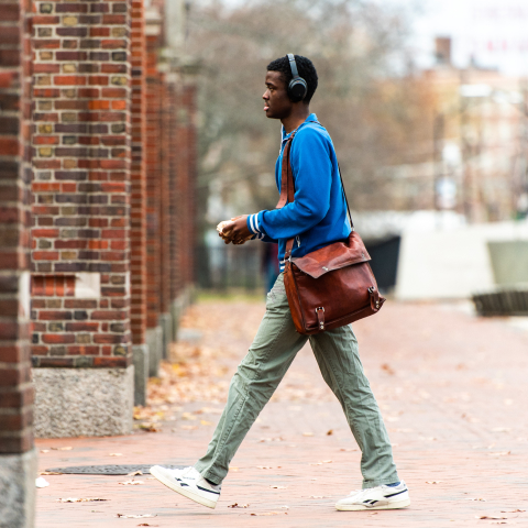 young student with headphones walking through a brick and mortar gate.