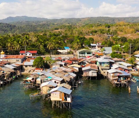 Aerial view of a fishing village with stilt houses over a nearby lake.