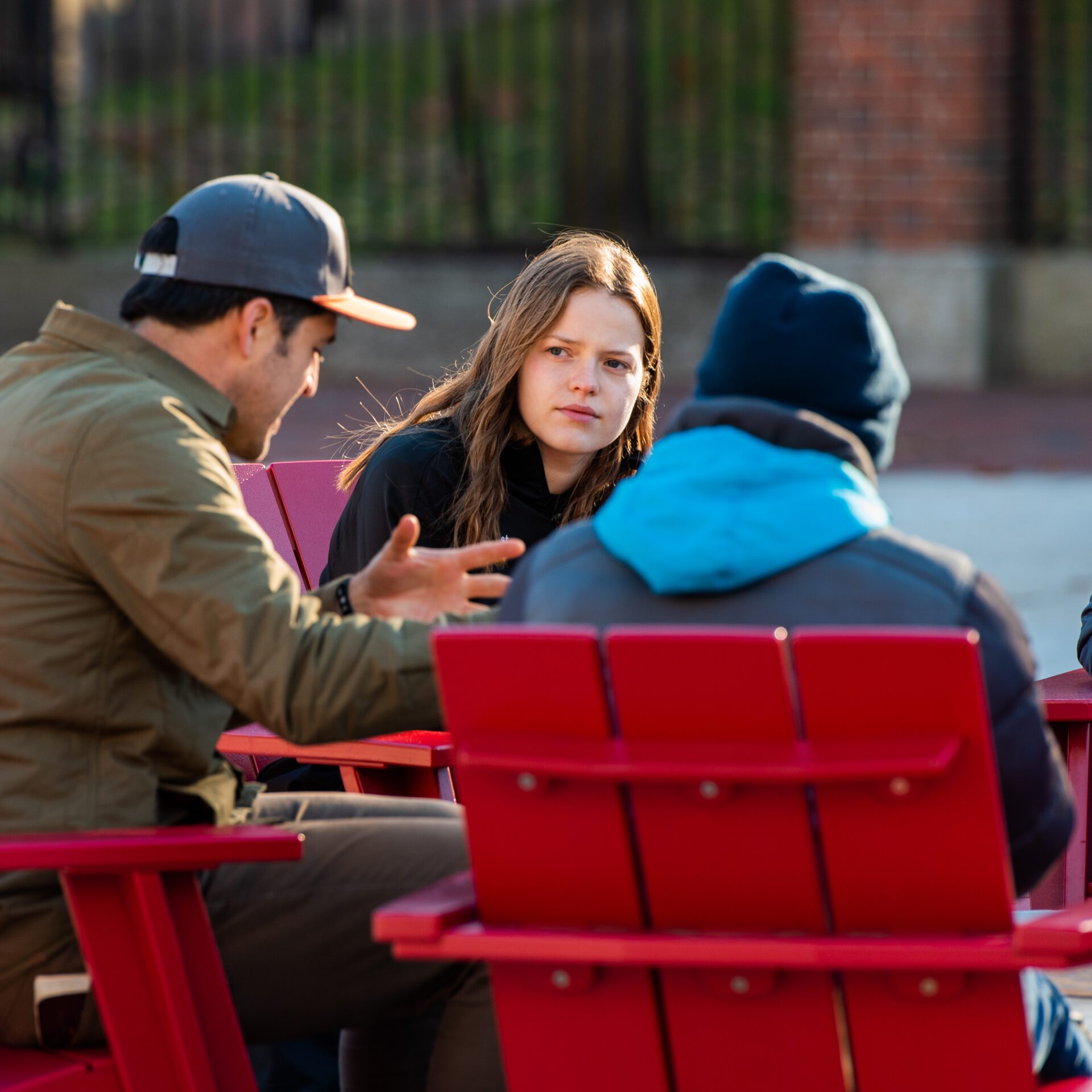 A group of students discussing something sitting outside on red chairs.