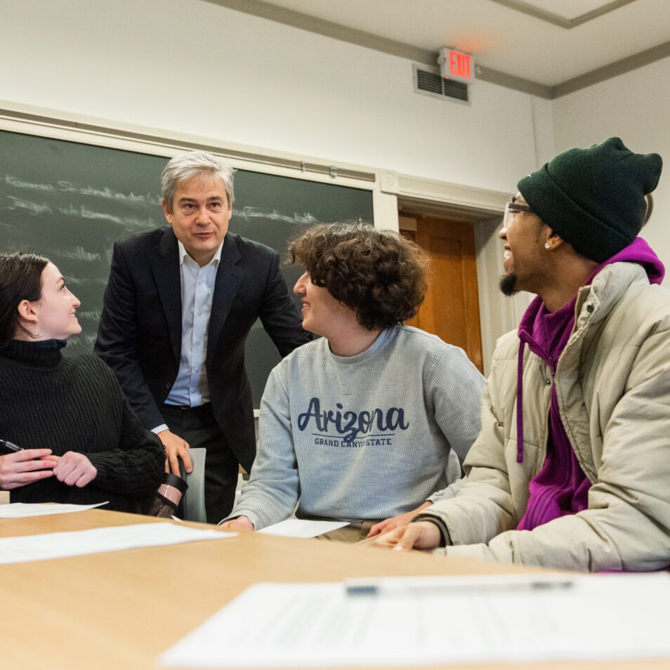 Students sitting at a table in a classroom interact with Professor Stephen Ansolabehere.
