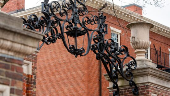 Image of a decorative iron archway above the brick gates to Harvard yard