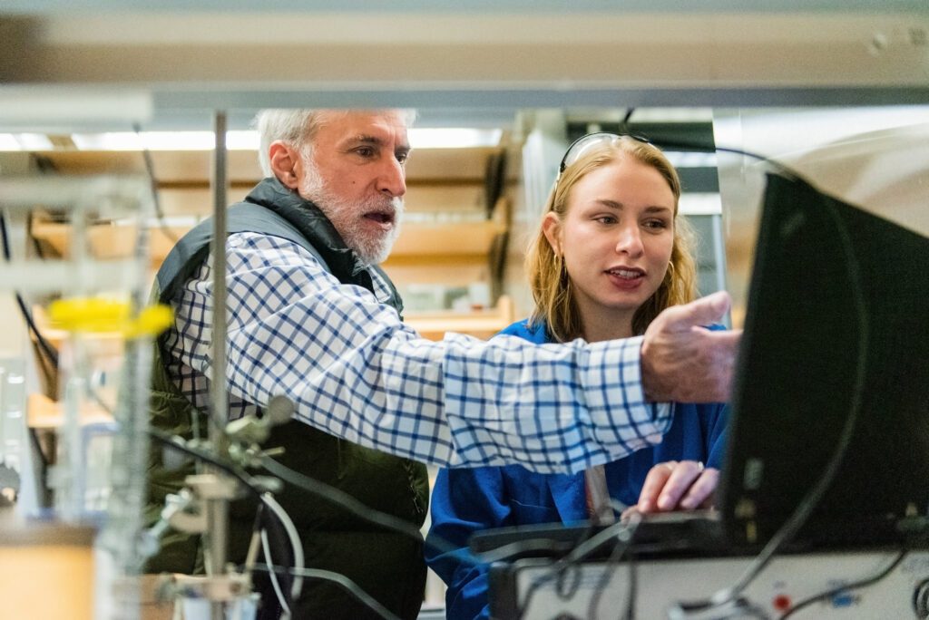 A professor and student in a chemistry lab. The professor is gesturing at a computer screen.