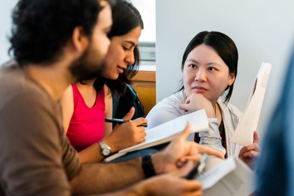 Three people holding papers and notebooks in discussion