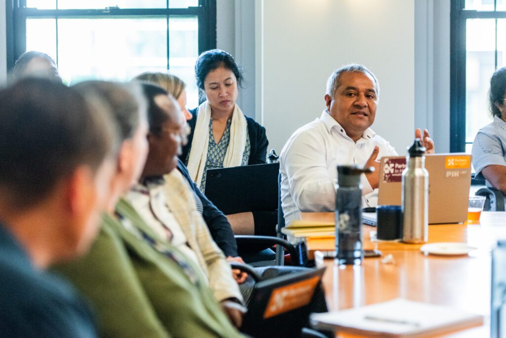 A global health researcher sits at a table during the workshop, gesturing as he speaks.