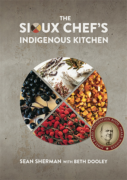 Book title reads: The Sioux Chef's Indigenous Kitchen. Sean Sherman with Beth Dooley. A round graphic reads James Beard Foundation Book Award Winner. On the cover, four "slices" of a circle show different food items including dark berries, red berries, root vegetables, and herbs.