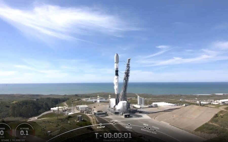 A rocket on a launch pad begins to take off. Ocean in the background.
