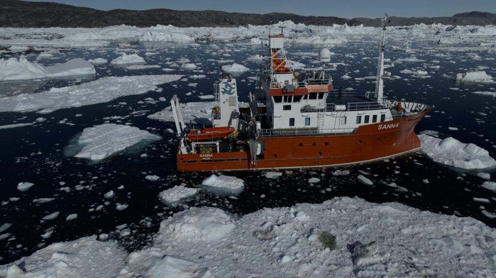 A red and white research vessel in the ice-strewn sea off of west Greenland. 