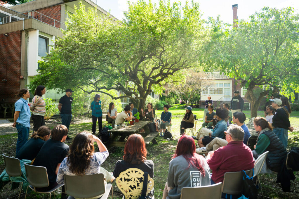 seed blessing ceremony participants sit in a circle of chairs under trees in the grove next to the HDS garden 