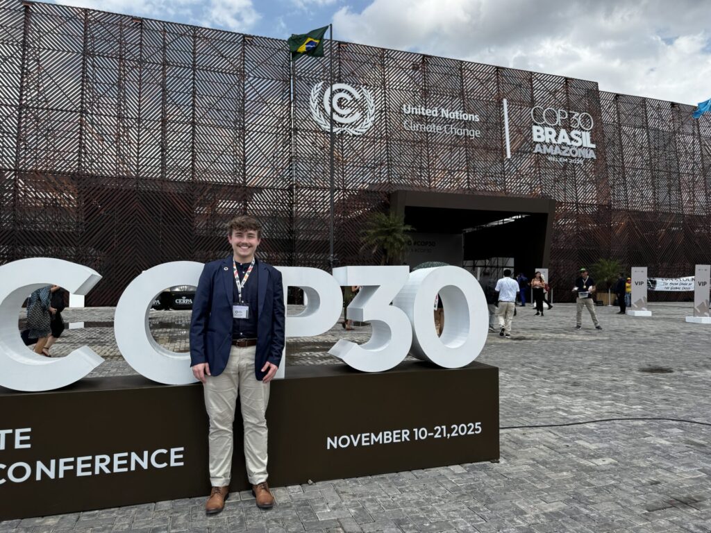 Harvard Student stands in front of the COP30 event venue sign in Belem Brazil.